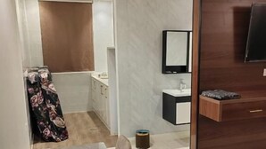 A modern hotel room with a marble dining table, a wooden cabinet with a TV, and a bathroom visible in the background.