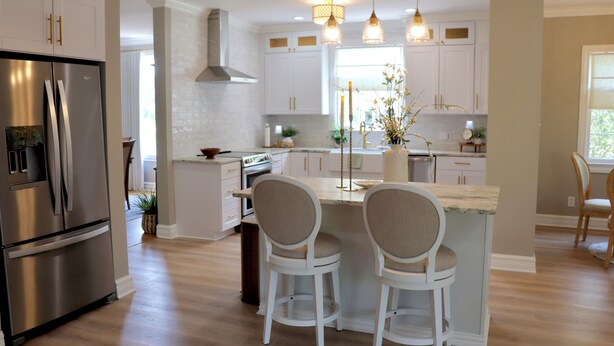 Una cocina moderna con armarios blancos, electrodomésticos de acero inoxidable y una isla central con dos taburetes de bar.