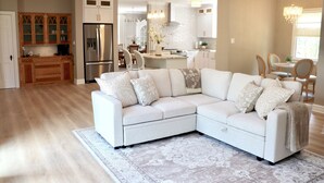 Una sala de estar moderna con un sofá modular, una cocina con armarios blancos y un comedor con una araña.