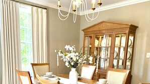 Comedor con una mesa de madera dispuesta para seis comensales, rodeada de sillas, una araña y un mueble de madera grande con puertas de cristal.