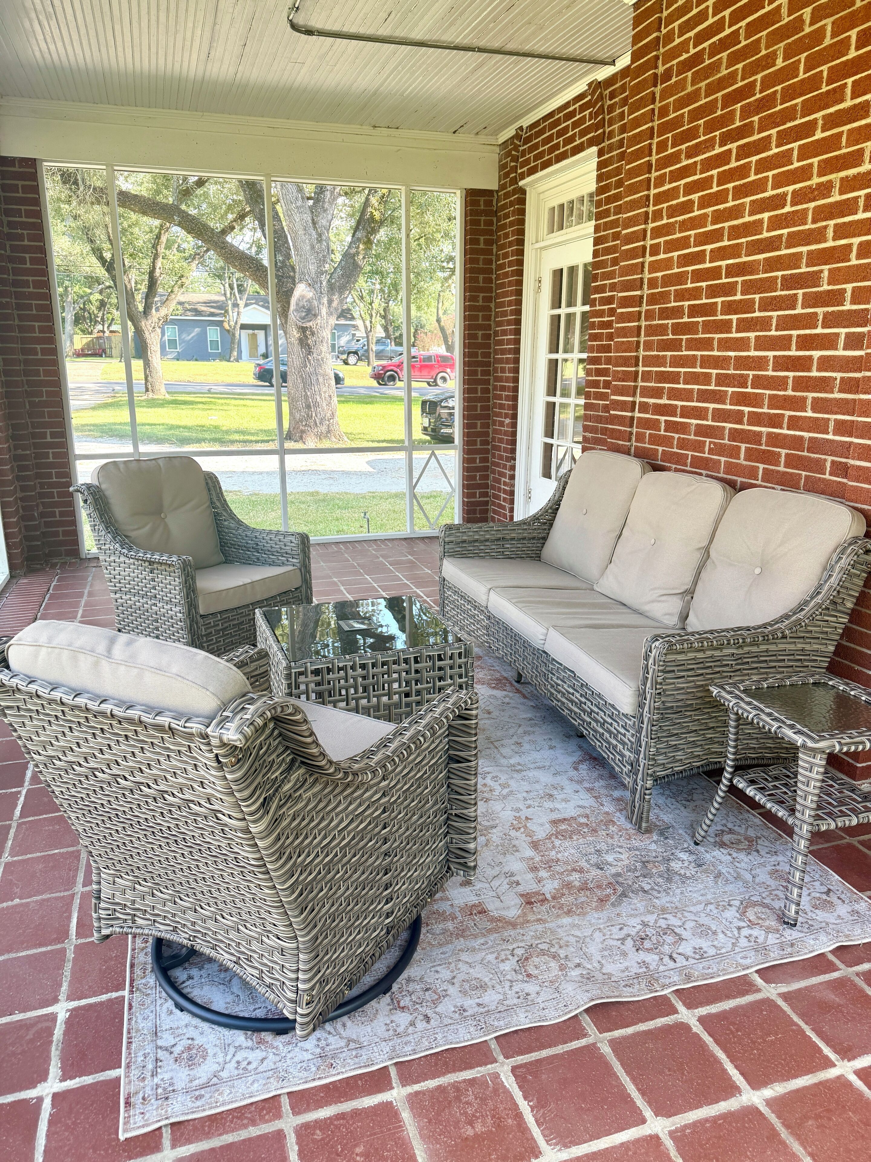 A covered patio area with wicker furniture, including a sofa and chairs, and a glass coffee table.