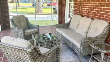 A covered patio area with wicker furniture, including a sofa and chairs, and a glass coffee table.