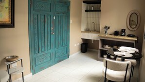 A kitchen with a turquoise door, a sink, a round table with chairs, and a small shelf with kitchen items. - El Inn de la Moderna (San Pedro Sula)