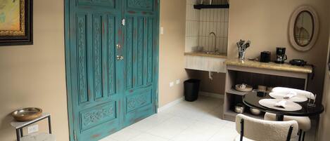 Une cuisine avec une porte turquoise, un évier, une table ronde avec des chaises et une petite étagère contenant des ustensiles de cuisine.