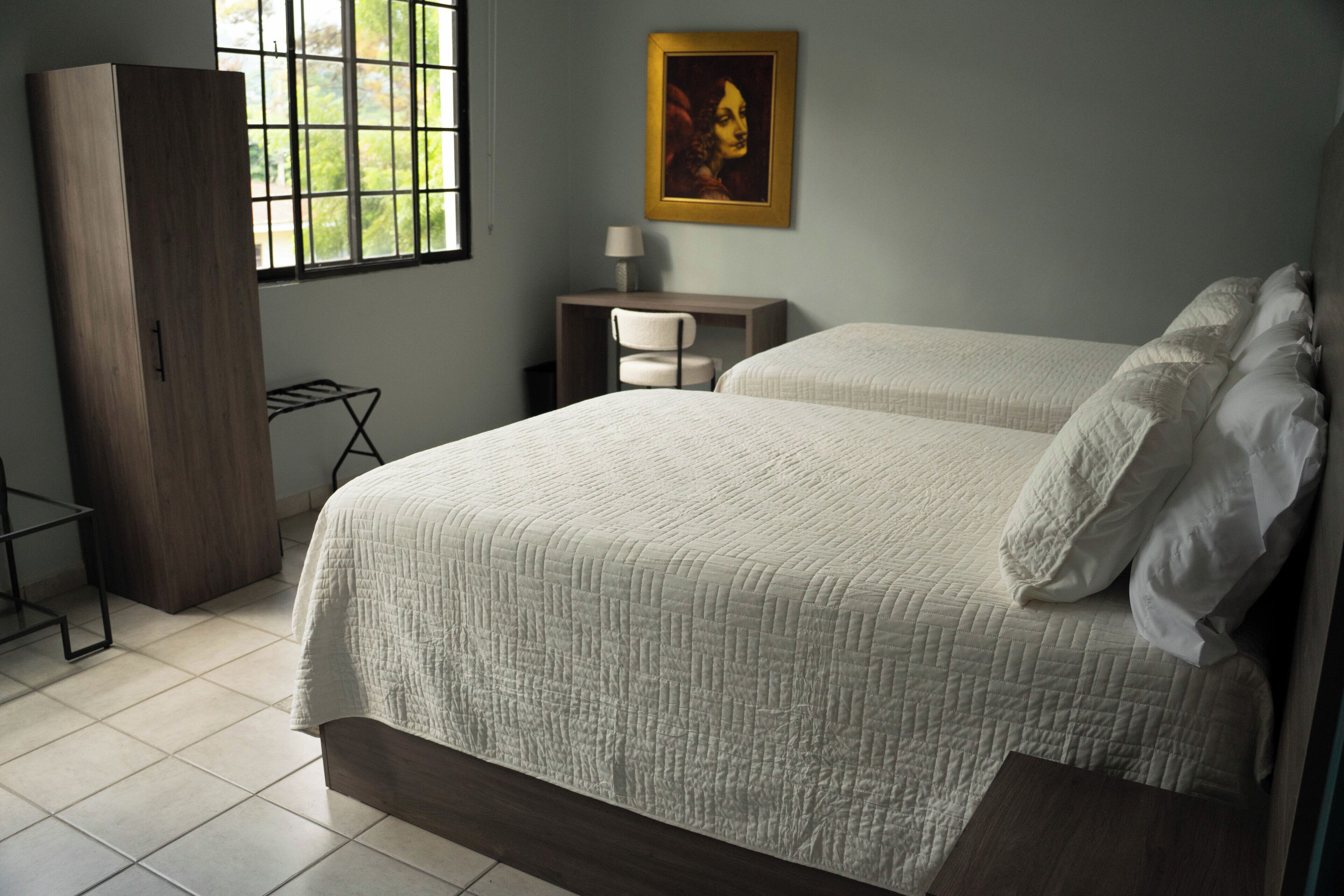 A bedroom with a large bed, a wardrobe, a desk with a chair, and a window with bars.