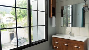 A bathroom with a large window, a sink, wooden cabinets, and a mirror. - El Inn de la Moderna (San Pedro Sula)