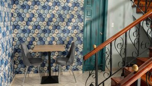 A dining area with a table and chairs, a teal door, and a staircase with a wooden handrail. - El Inn de la Moderna (San Pedro Sula)