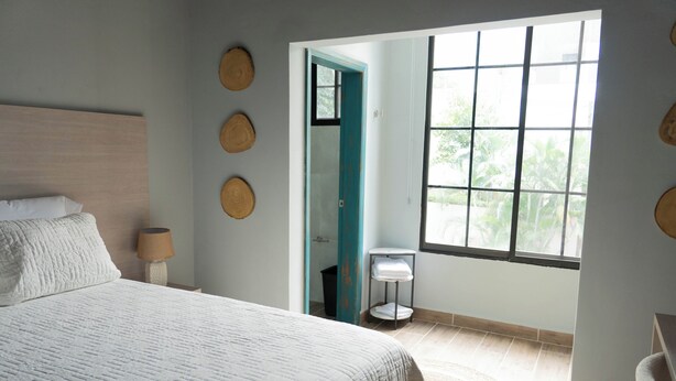 A bedroom with a large bed, a window, and a door leading to a bathroom. - El Inn de la Moderna (San Pedro Sula)