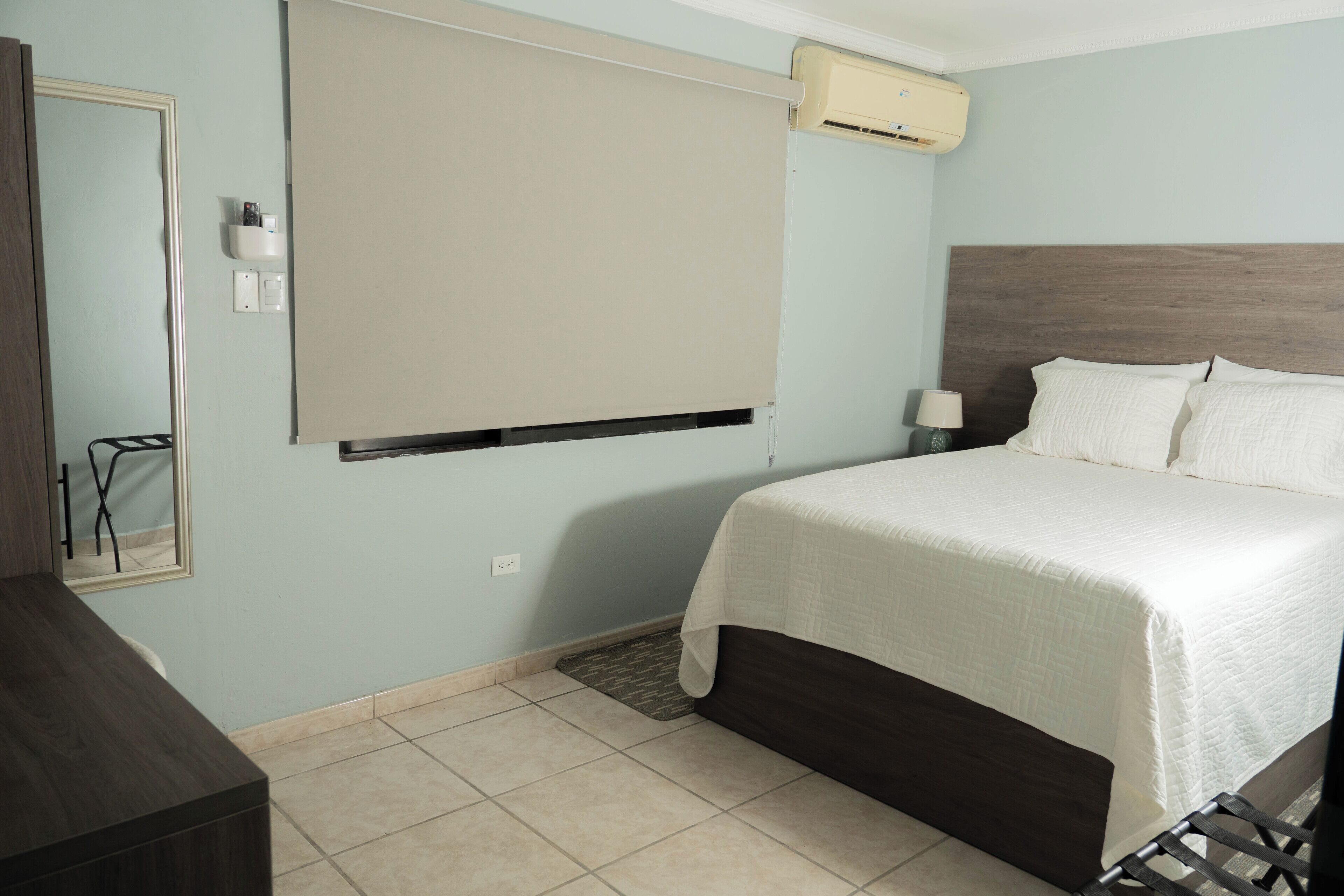 A bedroom with a bed, a bedside table, a mirror, and a wall-mounted air conditioner.