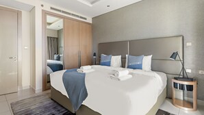 Una habitació d'hotel moderna amb un llit gran, un armari, un mirall i una taula de nit amb una làmpada.