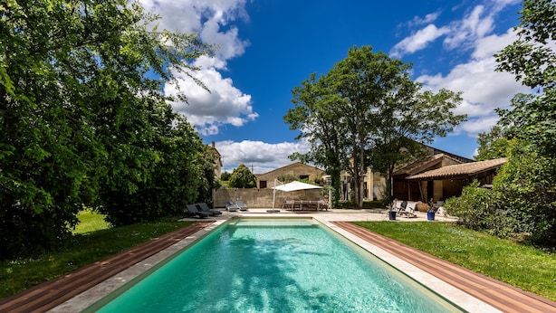 Una piscina rectangular con cubierta de madera, rodeada de follaje y un cielo azul despejado.