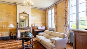 Una habitación con un piano, un globo terráqueo, un sofá, una araña y un amplio ventanal con cortinas.