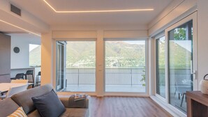 Un salon moderne doté d’une grande porte-fenêtre coulissante donnant sur un balcon avec vue sur les montagnes.