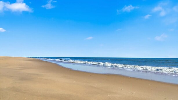 A wide sandy beach with gentle waves and a clear blue sky.