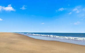 A wide sandy beach with gentle waves and a clear blue sky.