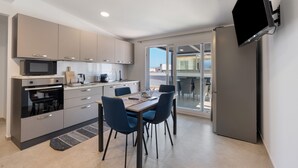 Une cuisine moderne avec un coin repas, un téléviseur à écran plat fixé au mur et une porte-fenêtre coulissante donnant sur un espace extérieur.