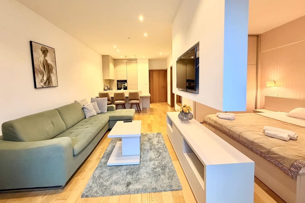 Uma sala de estar moderna com um sofá verde, uma mesa de centro e uma TV fixada na parede.