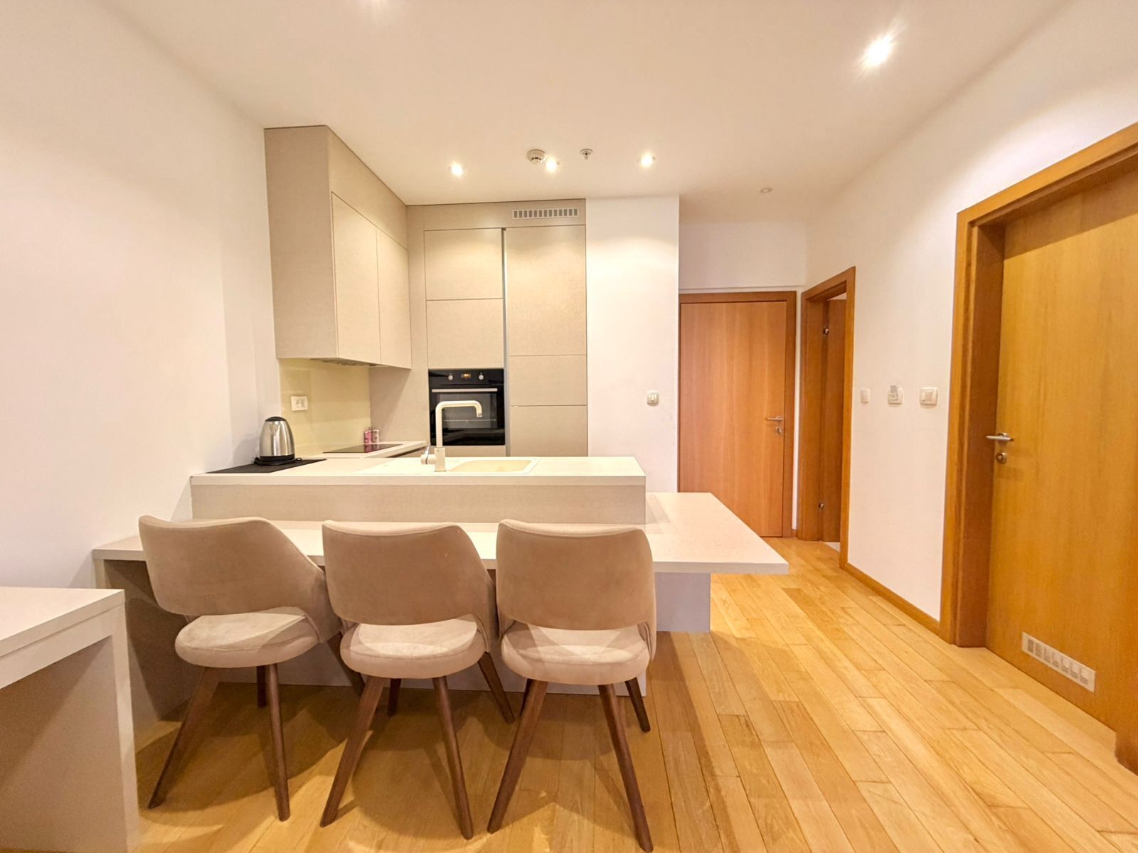 A modern kitchen with a central island, three chairs, and wooden flooring.