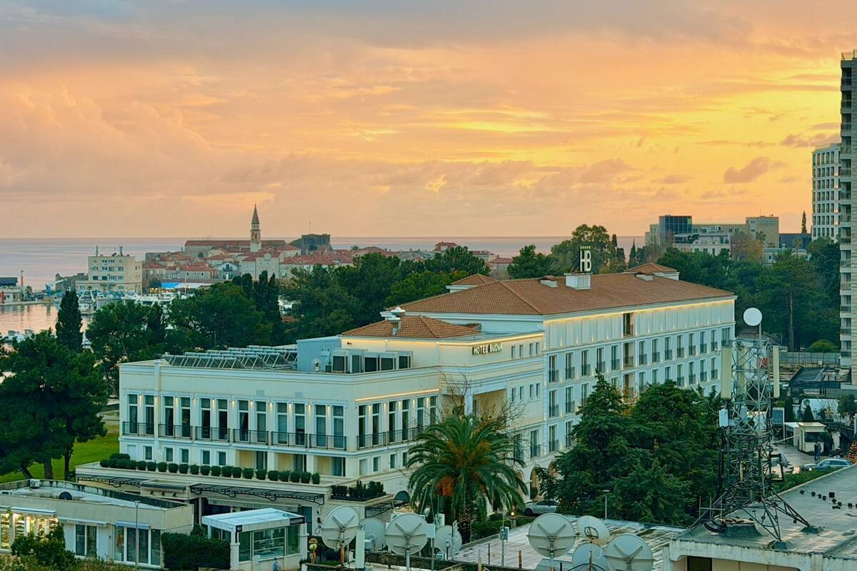 Um hotel moderno com telhado plano, vários andares e antenas parabólicas no telhado.