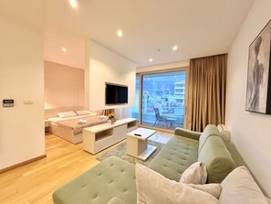 Een moderne hotelkamer met een bed, een bank, een televisie en een balkon met uitzicht op de stad.