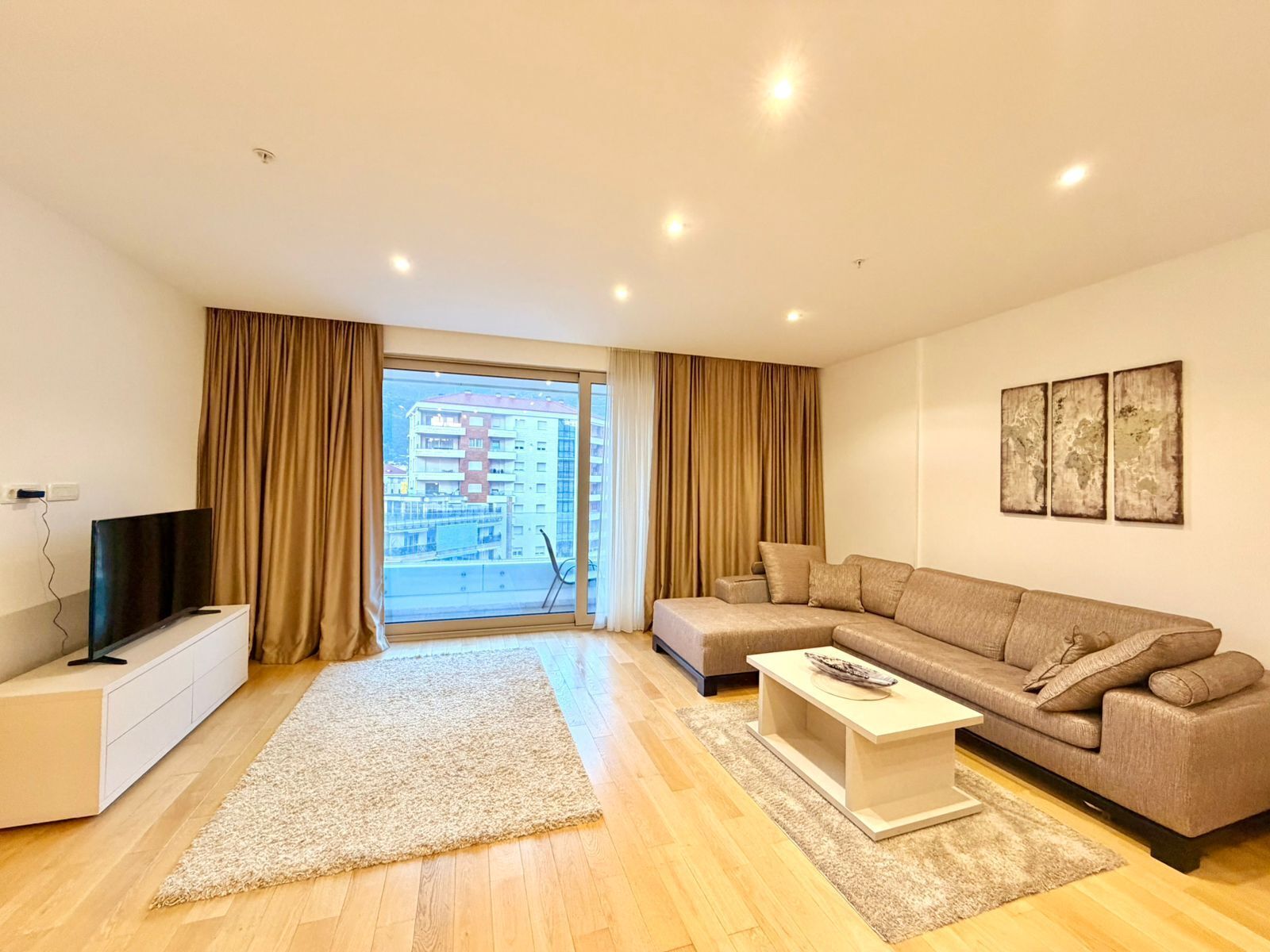 A modern living room with a large window, a sofa, a coffee table, and a TV on a stand.
