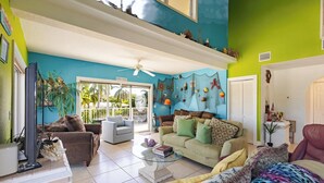 A spacious living room with a high ceiling, a ceiling fan, a large window, and a view of the outdoors. - Conch Nation – 4 Bedroom / 3 Bath Gulfside Home with Dockage (Marathon)