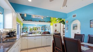 A kitchen with a dining area, featuring a central island, white cabinets, and a ceiling fan. - Conch Nation – 4 Bedroom / 3 Bath Gulfside Home with Dockage (Marathon)