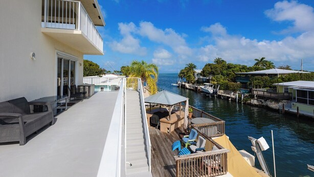 A waterfront property with a balcony, outdoor seating, and a view of the marina. - Conch Nation – 4 Bedroom / 3 Bath Gulfside Home with Dockage (Marathon)