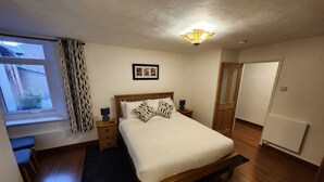 Une chambre à coucher avec un lit en bois, une table de chevet, une lampe, un tableau encadré au mur et une fenêtre avec des rideaux.