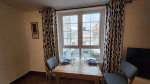 Un'area pranzo con un tavolo di legno, due sedie e una finestra con tende a motivi geometrici.