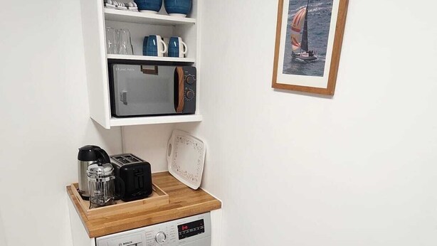 Un angolo lavanderia funzionale con lavatrice Bosch, forno a microonde e ripiano con stoviglie e bicchieri blu.