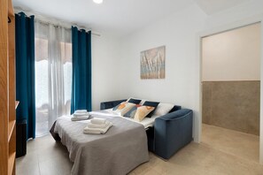 Habitación de hotel moderna con cama, sofá, un cuadro y vistas al exterior.