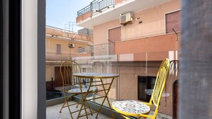 A balcony with yellow chairs and a table, a building with balconies and windows, and an air conditioning unit. - Room 'Camera 1 - P2' with Balcony, Wi-Fi and Air Conditioning (Balestrate)