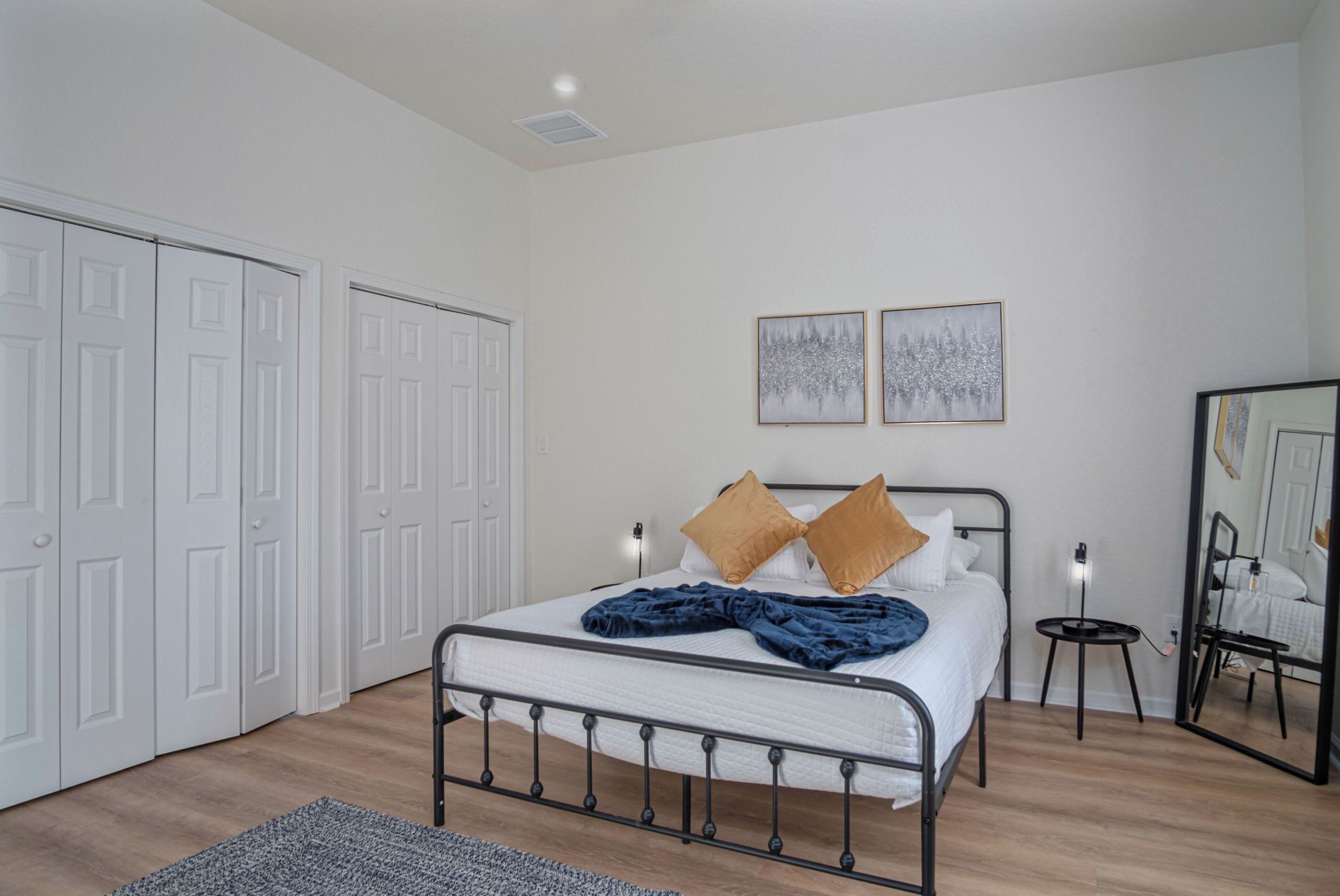 A bedroom with a bed, white walls, a mirror, and two framed pictures on the wall.