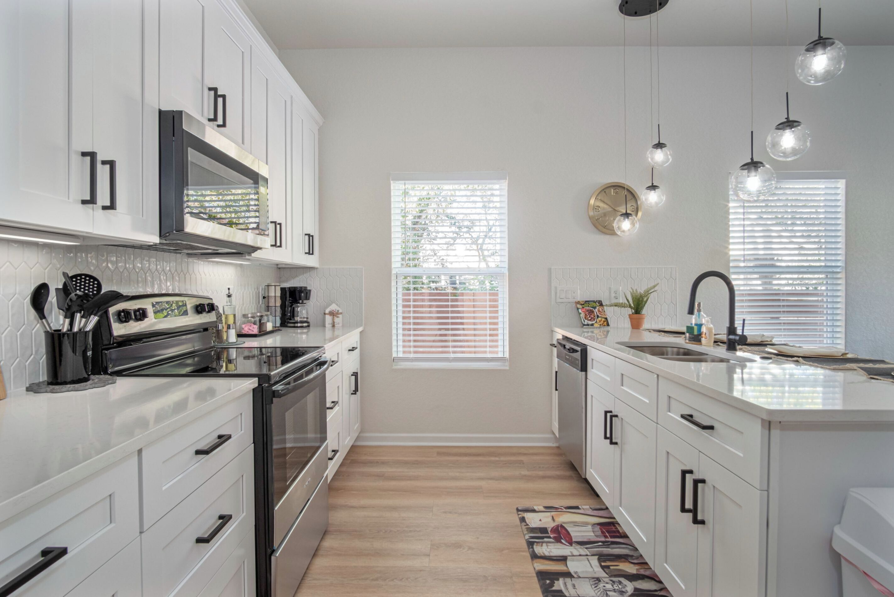 A modern kitchen with white cabinets, stainless steel appliances, and pendant lighting.