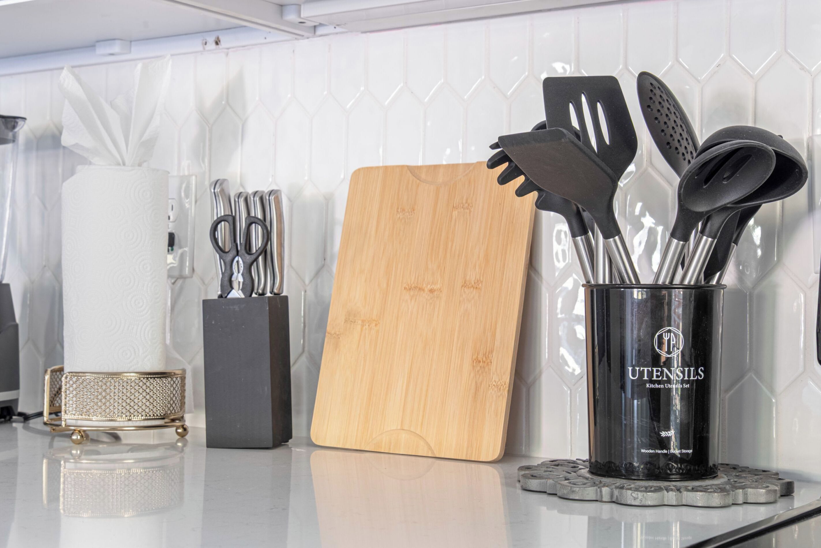 A kitchen counter with a cutting board, a canister of utensils, and a roll of paper towels.
