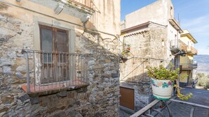 A stone building with a balcony, a potted plant, and a view of the surrounding area. - Apartment 'Le Case di Gilda' - Castiglione di Sicilia (Castiglione di Sicilia)