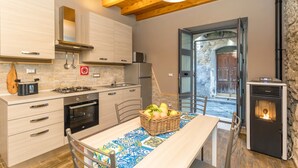 A kitchen with wooden cabinets, a stove, and a dining table with a basket of fruit. - Apartment 'Le Case di Gilda' - Castiglione di Sicilia (Castiglione di Sicilia)