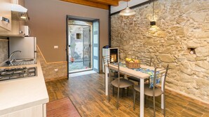 A modern kitchen with a stone wall, wooden ceiling, and a dining area with a table and chairs. - Apartment 'Le Case di Gilda' - Castiglione di Sicilia (Castiglione di Sicilia)