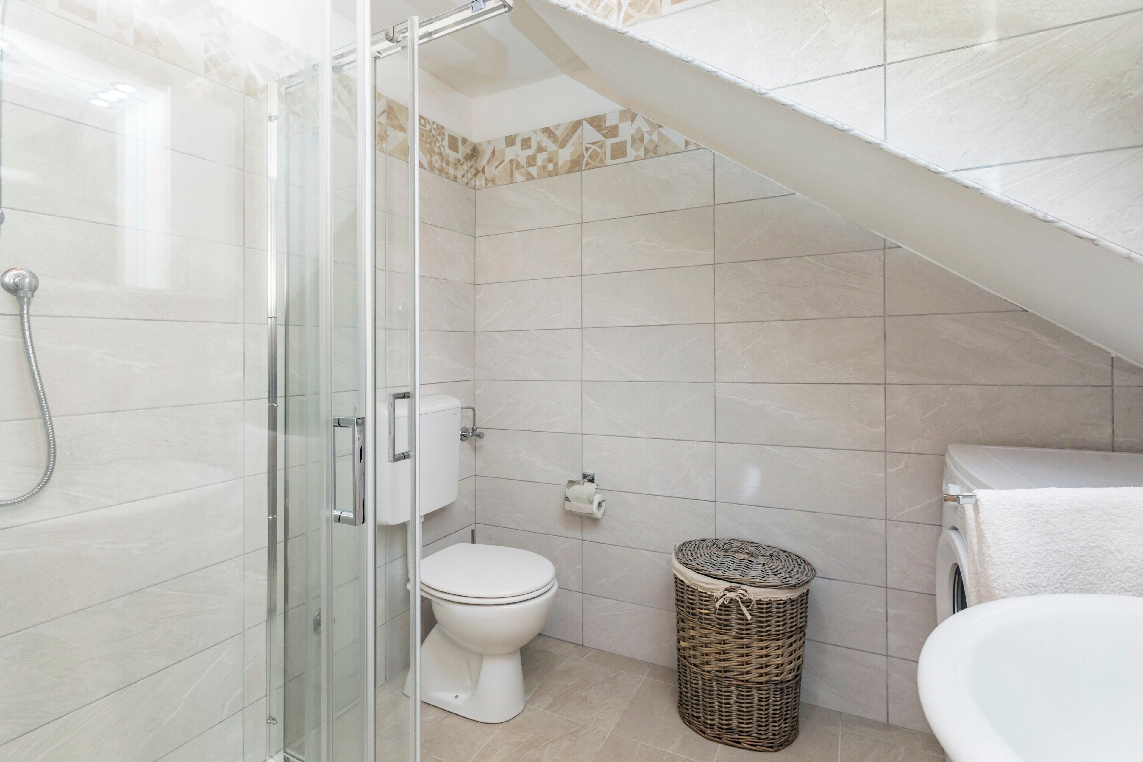 Une salle de bain avec une douche à parois de verre, des toilettes, un lave-linge et un panier en osier.