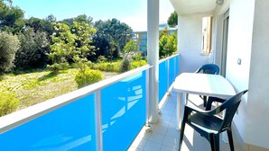 A balcony with a table and chairs, a view of greenery and buildings, and a blue railing. - COND. PELICAN - B2 5+1 - B80A4R (Bibione Pineda)