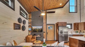 Un intérieur moderne avec un plafond en bois, une cheminée, une cuisine équipée d’appareils électroménagers en acier inoxydable et un coin repas avec une table et des chaises en bois.