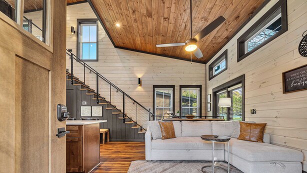 Un vaste espace de vie doté d’un plafond en bois, d’un canapé moderne, d’une petite table ronde et d’un escalier menant à un niveau supérieur.