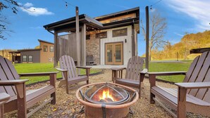 En patio med Adirondack-stole, bålsted og en bygning i sten i baggrunden.