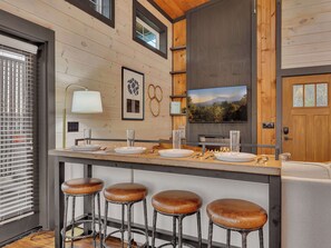 Une cuisine moderne avec un plan de travail en bois, des tabourets de bar, un téléviseur et une cheminée.