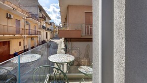 Een smalle straat met gebouwen aan beide zijden, een glazen balustrade en twee ronde tafels met stoelen.