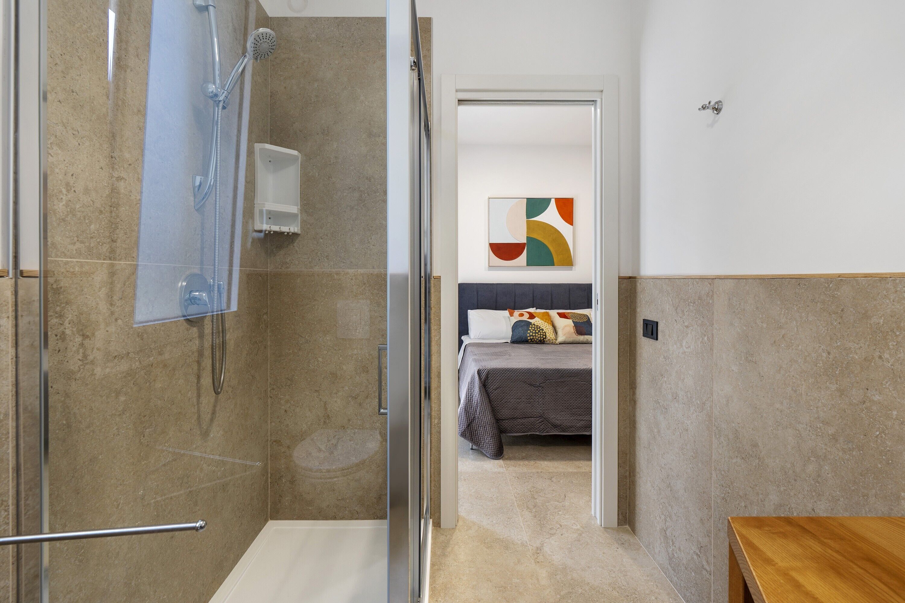 Een badkamer met een douche, een glazen deur en een bed in de aangrenzende kamer.