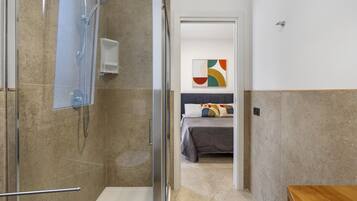 Een badkamer met een douche, een glazen deur en een bed in de aangrenzende kamer.