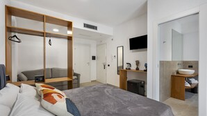 Een moderne hotelkamer met een bed, een houten kledingkast, een televisie, een badkamer met een wastafel en een klein bureau.