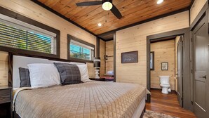 A bedroom with a bed, a ceiling fan, a window with blinds, a bedside table, a wall-mounted light, and a door leading to a bathroom. - Fab New 2 Level Build I Fire Pit I Private Hot Tub I Game Room (Sevierville)